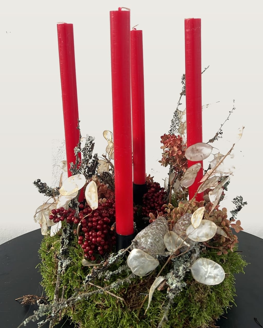 Adventskranz auf Moos mit vier roten Kerzen, Beeren, Silberblatt und Flechten